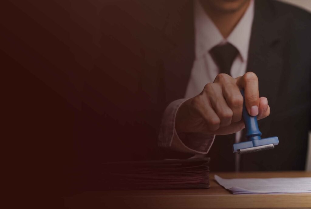 A hand in a suit pressing a rubber stamp onto a document at a desk
